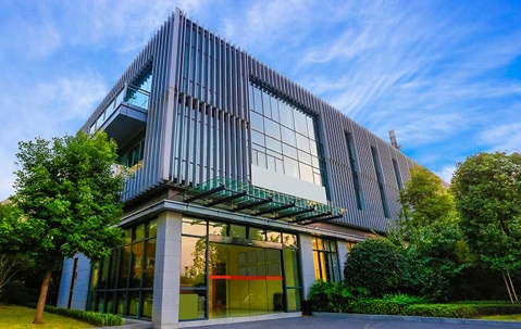 Large glass and steel commercial building surrounded by green trees.